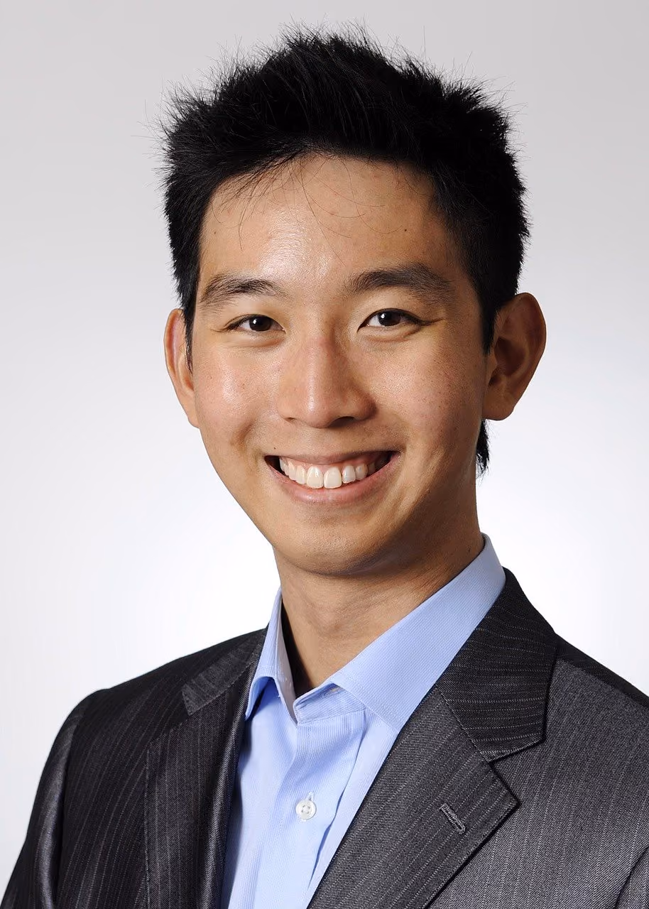 After: Smiling man in a grey blazer and blue shirt against a light grey backdrop