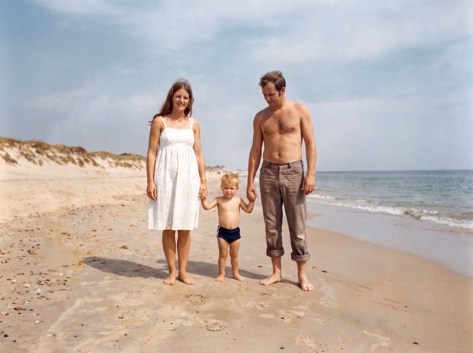 After: Couple holding the hands of a toddler on a sandy beach, restored from a cracked and faded print