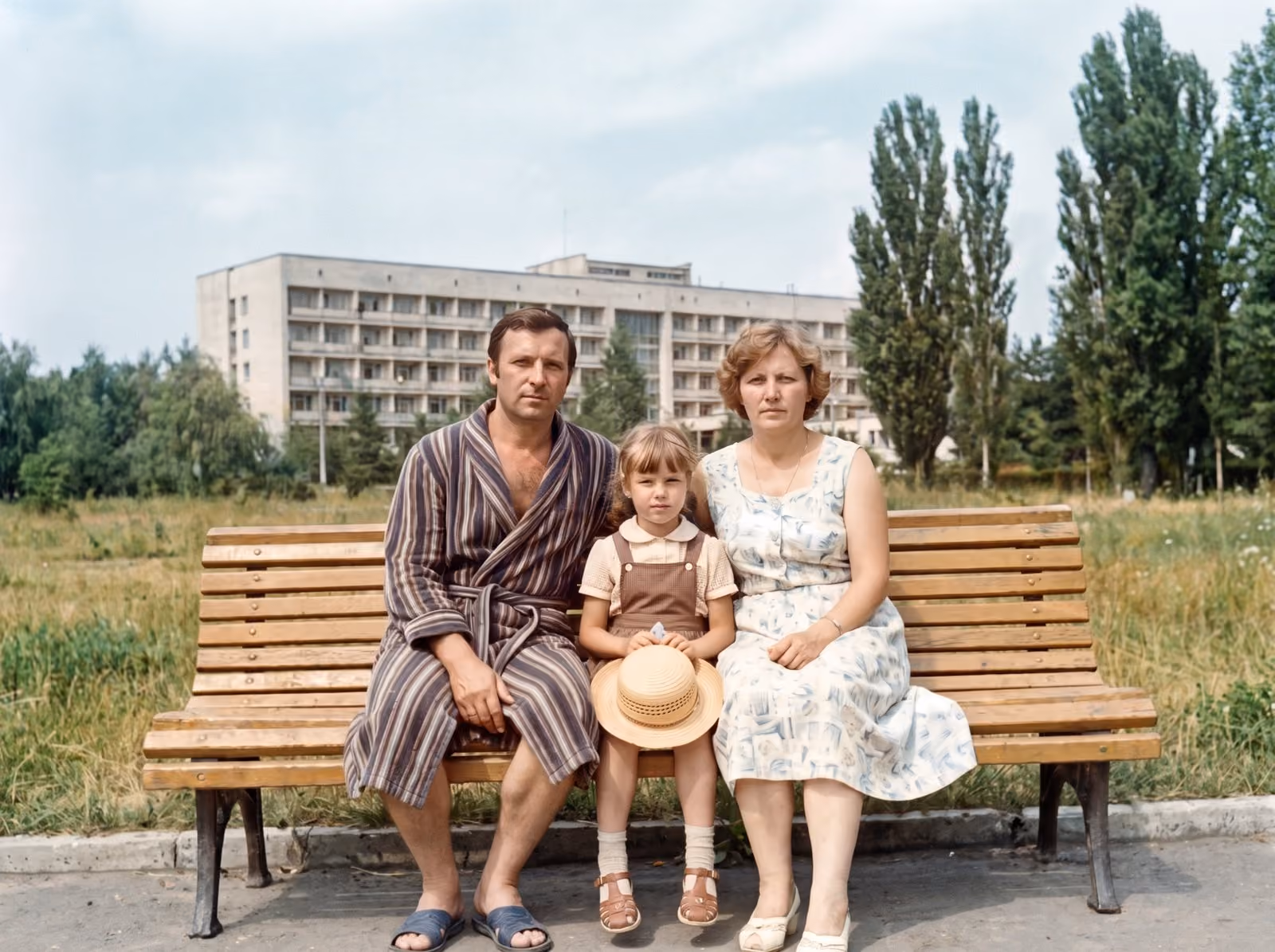 After: Parents and their daughter on a bench in front of a resort building, restored from a spotted and creased print