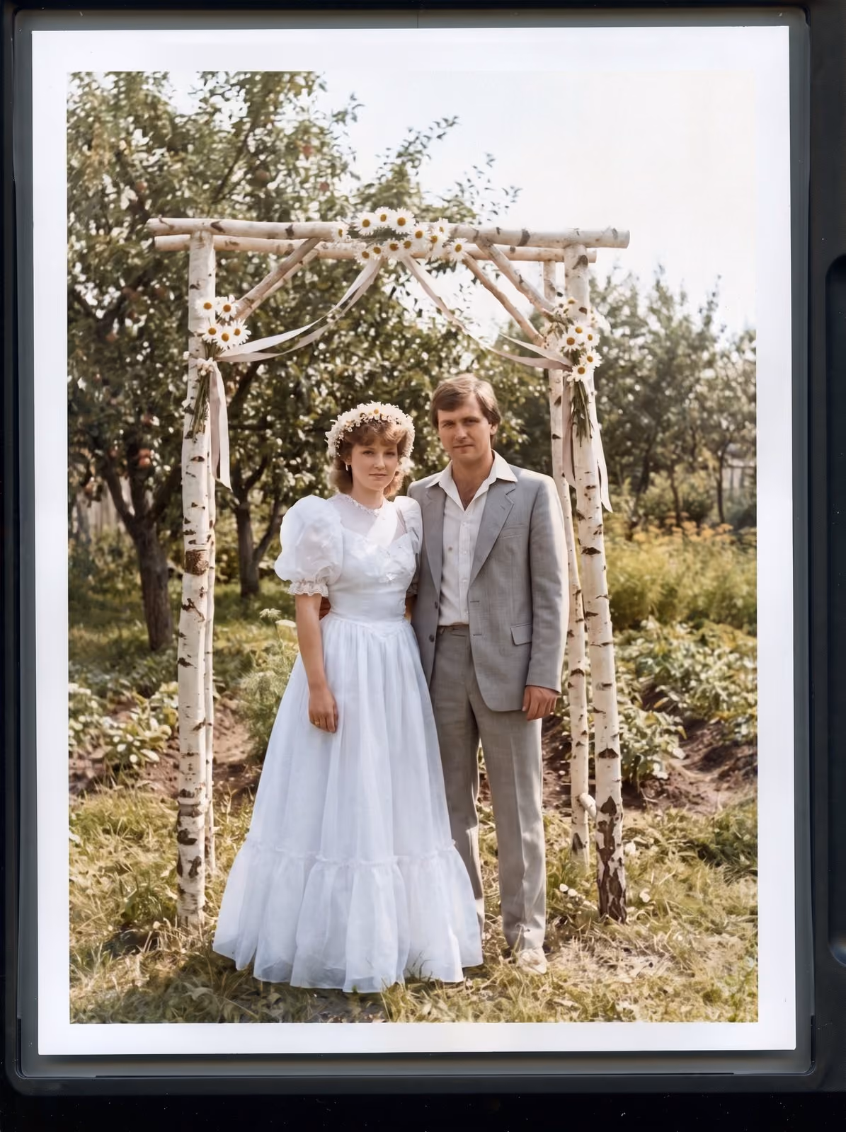 After: Bride and groom standing under a birch arch in an orchard, restored from a torn and stained print