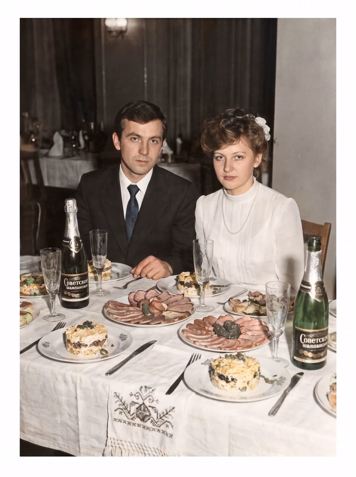 After: Bride and groom seated at a festive table with champagne, restored from a creased and stained print