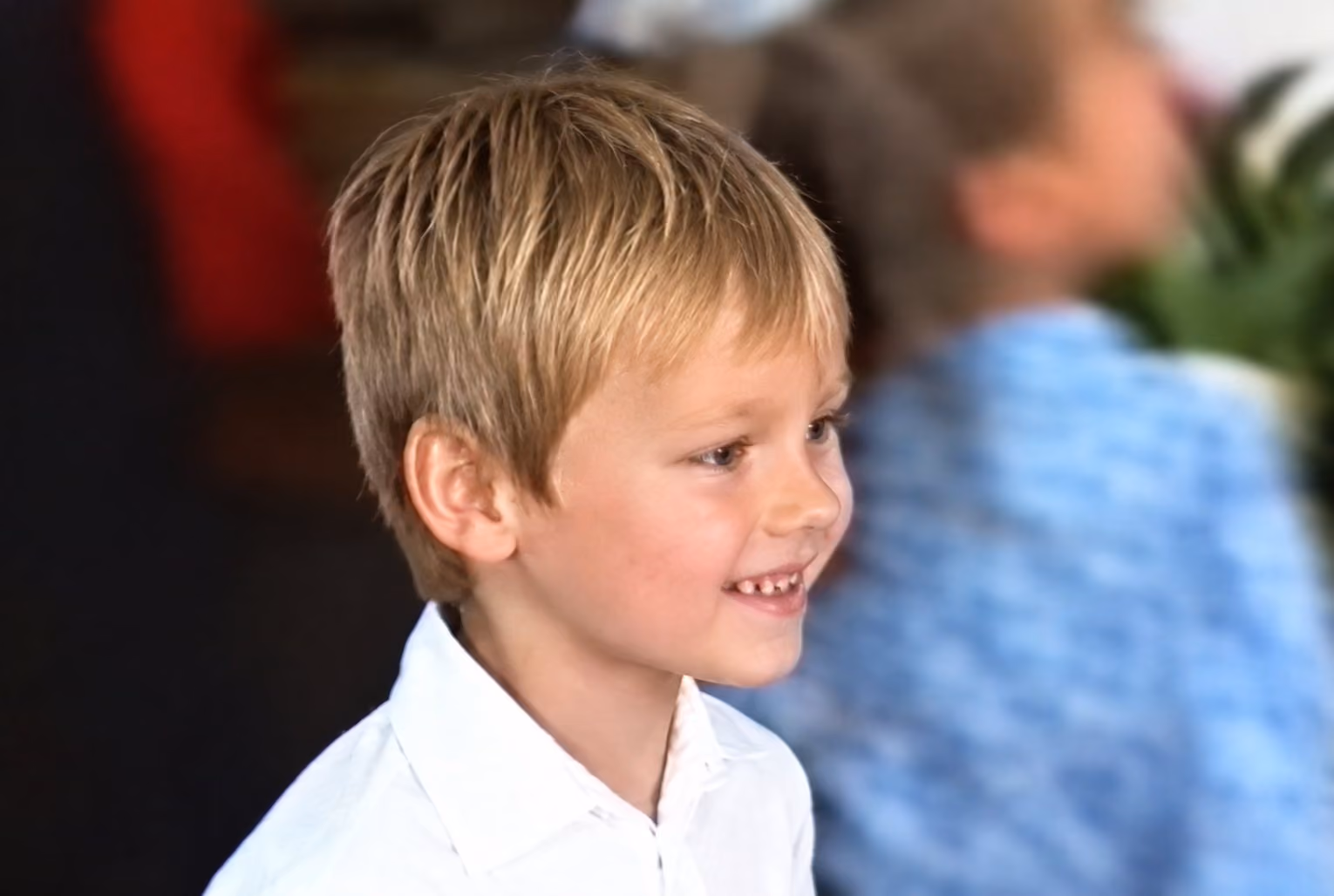 After: Close portrait of a smiling blond boy in a white shirt, enhanced from a soft, low-resolution frame