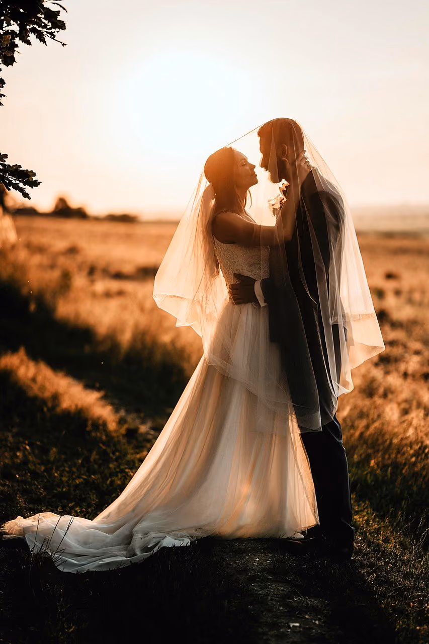 After: Bride in a veil and groom embracing in a field at golden hour