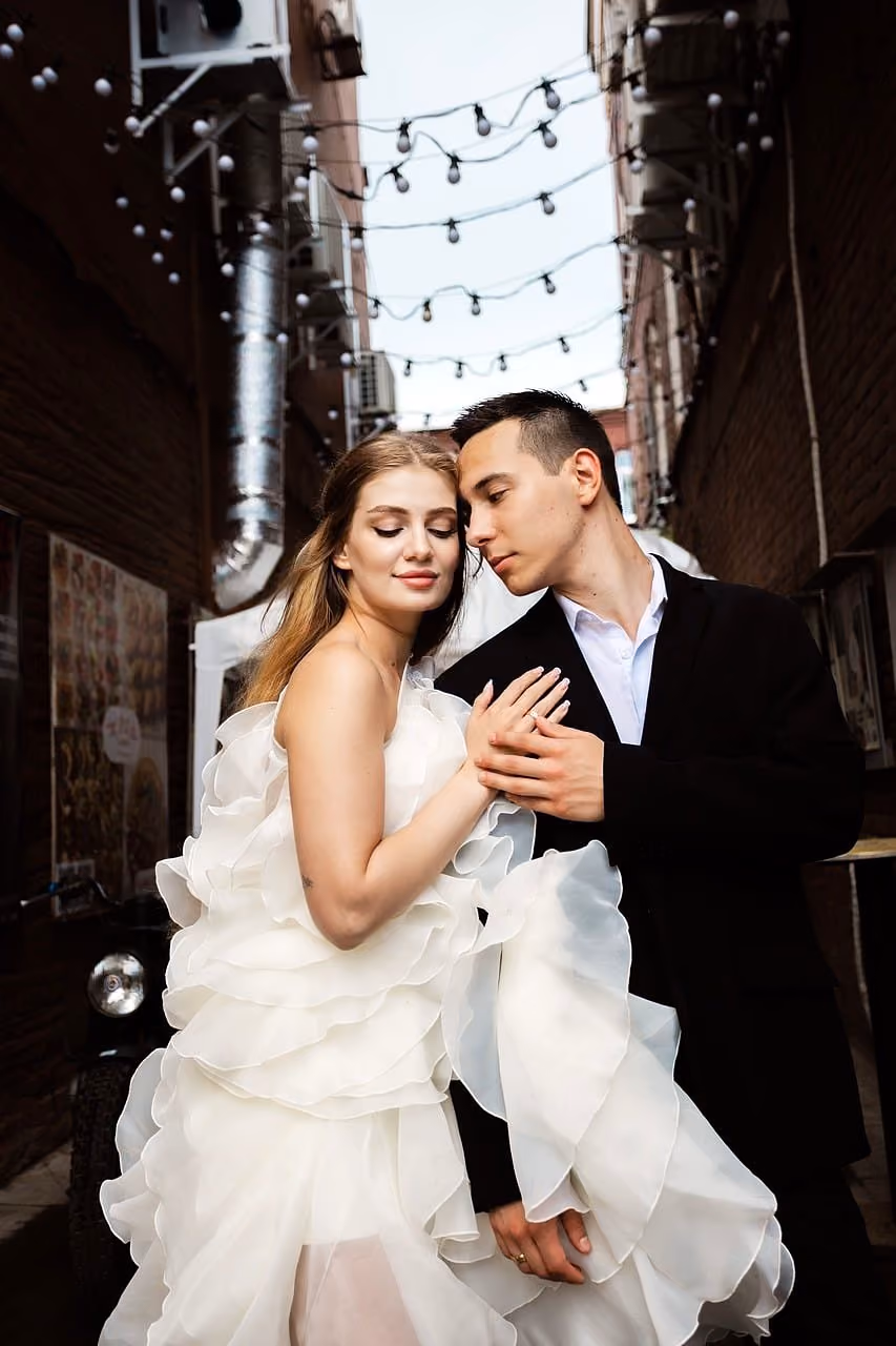 After: Bride in a voluminous gown and groom embracing in a narrow street with string lights